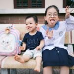 Happy children sitting on a bench making funny faces, creating playful memories.