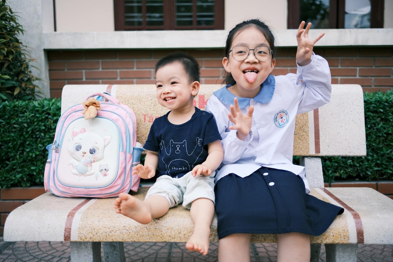 Happy children sitting on a bench making funny faces, creating playful memories.